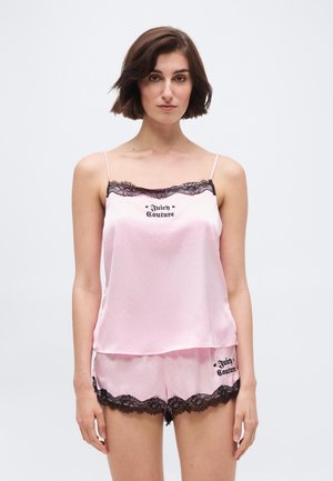 Naine kannab heleroosa satiinist kamisoolit ja lühikeste pükstega pidžaama komplekti, millel on musta pitsi ääris ning peal ja pükstel on kiri "Juicy Couture".