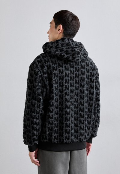 Black faux fur hoodie with textured pattern, oversized fit, and drawstring hood. Ribbed cuffs and hem, worn over gray pants.