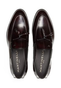 Mocasines de cuero en un burdeos profundo, con un acabado suave, borlas decorativas y marca en relieve en las plantillas negras.