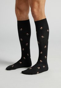 Sorte knæstrømper i knælængde med gentaget mønster af små peberkagefigurer iført røde hatte, lavet af blødt, strækbart stof.