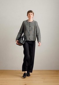 Γκρι ριμπ ανοιχτό μπλουζάκι με κουμπιά μπροστά, συνδυασμένο με μαύρες φαρδιές παντελόνες και μαύρα παπούτσια, αξεσουάρ με μια μαύρη τσάντα.