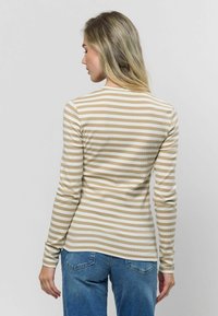 Garums piedurknēm krekls ar horizontālām bēšām un baltām svītrām, ribota faktūra, apaļa kakla izgriezuma forma, valkāts ar gaiši ziliem džinsiem.