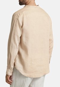 Camicia di lino beige chiaro con maniche lunghe, orlo arrotondato e polsini abbottonati. Presenta un colletto semplice e una vestibilità rilassata.