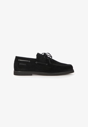Black suede men's boat shoe with lace-up front, moc toe stitching, and low rubber sole, shown in side profile on white background.