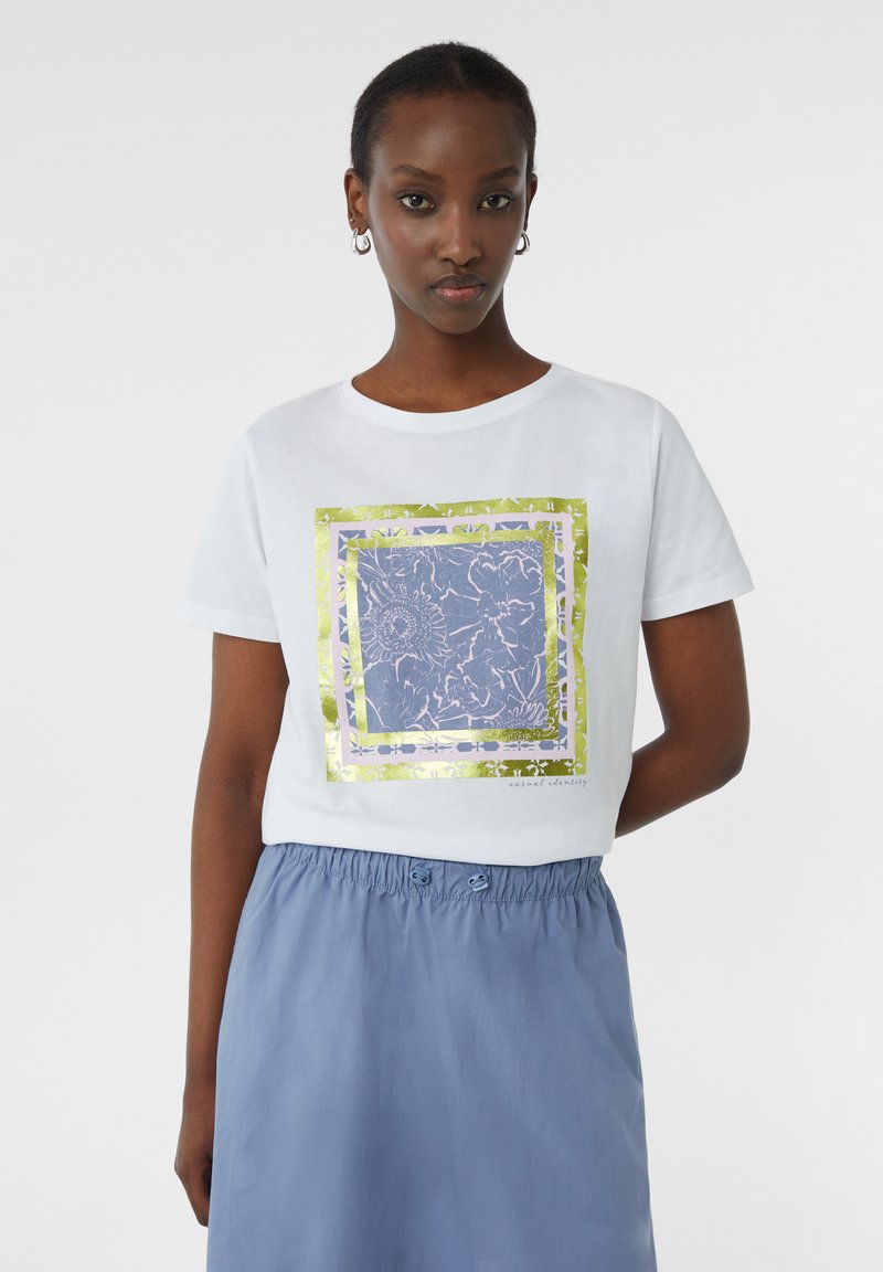 Witte katoenen t-shirt met een bloemig ontwerp in blauw en gouden folie-lijst; gecombineerd met een lichtblauwe rok met een trekkoord in de taille.