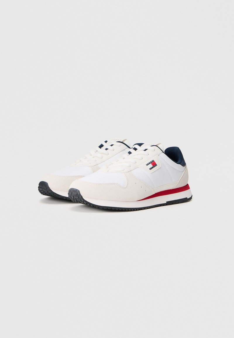 White athletic shoes with suede and mesh, navy accents, red stripe on sole, and rubber outsole with textured tread for traction.