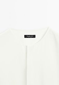 Bílá košile s kulatým výstřihem, vybavená knoflíkovou légou a štítkem se nápisem "Massimo Dutti". Hladká textura a ležérní design.