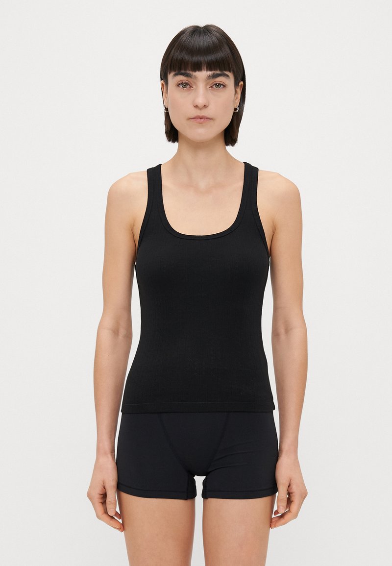 Fekete tank top bordás anyagból, széles pántokkal és lekerekített nyakkivágással, fekete rövidnadrággal párosítva. Simára szabott textúra, testhezálló dizájn.