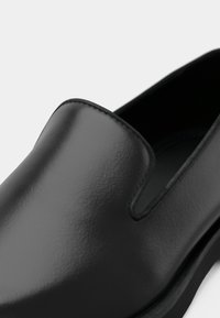 Sort slip-on sko med en glat finish, blød tekstur og subtile syninger langs kanterne. Rund tådesign.