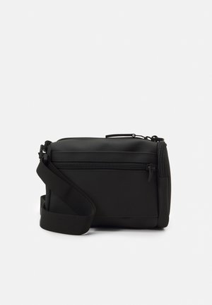 Sac bandoulière noir avec sangle réglable, poche zippée à l'avant et finition mate lisse sur un fond uni.