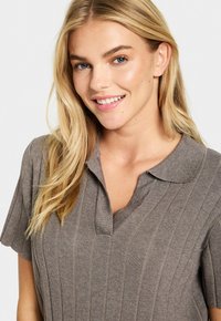 Grå ribbad polo-shirt med korta ärmar, en krage och en V-ringning. Tyget har en slät textur med subtila vertikala ränder.