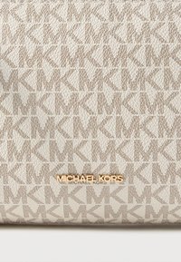 Beige håndtaske med tekstureret stof med et gentaget "MK" monogrammønster; guld "Michael Kors" logo i midten nederst.