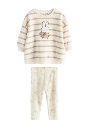 Dugi top krem i bež prugast s dizajnom zečića koji drži cvijeće, uparen s krem tajicama s ponovljenim uzorkom zečića i cvijeća.