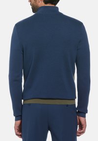Pull en maille bleu foncé avec un col montant, présentant des poignets et un ourlet côtelés, et un accent vert olive en bas.