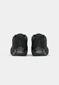 Zwarte sportieve schoenen met gestructureerde mesh bovenkanten, gebogen accenten, gevoerde kraag en gemusterde zolen, gezien vanuit de achterkant.