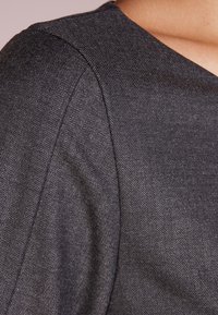 Texture de tissu chevron gris foncé avec de fines lignes diagonales, présentant une surface lisse et un détail structuré de couture d'épaule.