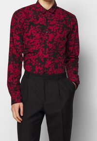 Zwarte shirt met een rood abstract patroon, button-down kraag, lange mouwen en zwarte knopen, gecombineerd met zwarte pantalon.