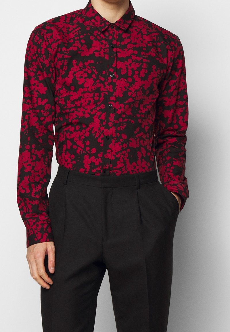 Zwarte shirt met een rood abstract patroon, button-down kraag, lange mouwen en zwarte knopen, gecombineerd met zwarte pantalon.