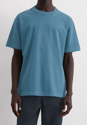 Koszulka z krótkim rękawem w stonowanym kolorze morskim, z okrągłym dekoltem i luźnym krojem. Gładka faktura z minimalnymi szwami.