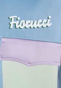 Tissu synthétique bleu clair avec une poche lavande ornée du logo « Fiorucci » en vert. Surface texturée avec des détails de couture contrastants.