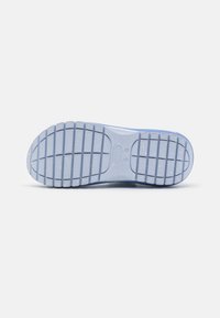 Semelle d'une chaussure violet clair avec un motif de bande de roulement rainuré et le nom de la marque en creux au centre, présentée sur un fond blanc uni.