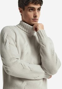 Ljust grått stickat polotröja med en strukturerad kabelmönster, ribbad krage och ärmar, med en lös och avspänd passform.