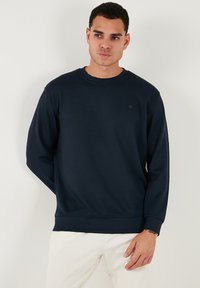 Felpa blu navy realizzata in tessuto testurizzato, con colletto rotondo, maniche lunghe e polsini a coste. Piccolo logo sul petto.
