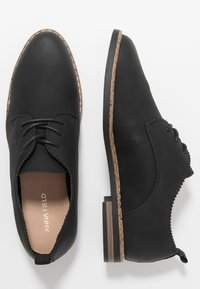 Chaussures noires en cuir avec une finition lisse, bout arrondi et des coutures discrètes. Elles présentent un petit talon et une bordure décorative en forme de scallop sur les côtés.