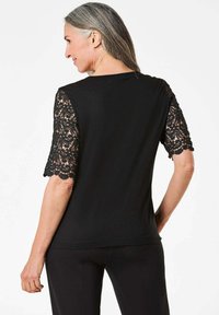 Zwart topje met kant korte mouwen, versierd met complexe bloemmotieven, gemaakt van zachte stof en met een strakke pasvorm, gezien vanuit de achterkant.