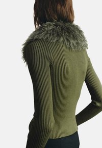 Suéter acanalado de color verde oliva con un alto cuello de piel sintética. Diseño ajustado, mangas largas y tejido texturizado.