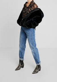 Zwarte nepbont bomberjack over een bruin luipaardprint top, gecombineerd met lichtblauwe opgerolde jeans en zwarte laarzen met slangenprint tot de enkel.