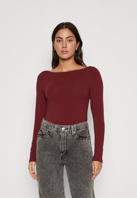 Burgunderfarget langermet bodysuit med bred hals. Kombinert med høytlivde, falmede svarte jeans. Glatt tekstur, slim fit design.