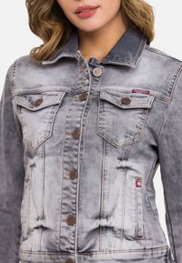 Grijze denimjack met een vervaagd ontwerp, voorzien van twee borstzakken, metalen knoopaccenten en verhoogde stiknaden langs de naden.