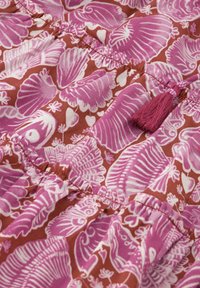 Roze bloemenstof met schelpen- en vispatronen op een bruine achtergrond, met verzamelde secties en een paarse franjesdetail.