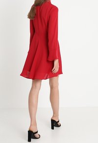 Rotes Kleid mit langen Ärmeln und einem ausgestellten Rock. Hergestellt aus leichtem Stoff, mit glatter Textur und tailliertem Design.