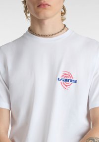 T-shirt bianco in cotone con logo blu "Vans" e design a spirale rossa sul lato sinistro del petto. Maniche corte e scollatura a girocollo.