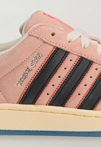 Różowy zamszowy sneaker z czarnymi i koralowymi paskami, perforacjami i teksturowaną kremową podeszwą środkową. Logo „PATRICK STAR” po boku.