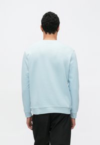 Felpa azzurro chiaro con scollo tondo, polsini e orlo a costine. Il tessuto sembra morbido con una texture liscia, abbinata a pantaloni neri.