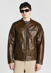 Giacca in pelle marrone con colletto alto, dettagli rigati sulle spalle e tasca frontale con zip. Texture liscia e design aderente.
