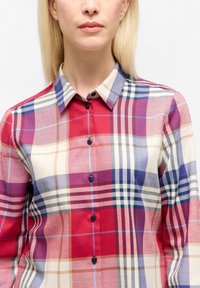Camicia a quadri rossa e crema con accenti blu navy e azzurro; presenta un colletto, maniche lunghe e bottoni neri lungo il davanti.