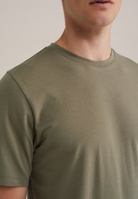 Camiseta verde oliva de manga corta en algodón suave con cuello redondo, que presenta una textura lisa y sin patrones ni elementos visibles.