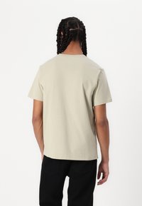 Camiseta de manga corta en un tono beige claro con cuello redondo, hecha de algodón suave. Presenta un corte recto y una textura suave.