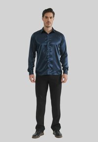 Chemise satin marine à manches longues avec un bouton à l'avant et un col, associée à un pantalon noir et des chaussures noires ; texture lisse, silhouette ajustée.