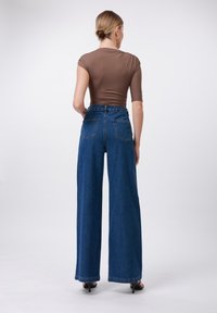 Šviesiai ruda prigludusi palaidinė derinama su aukšto liemens plačiomis mėlynomis džinsinėmis kelnėmis. Kelnėse yra dvi užpakalinės kišenės ir minimalizmo stilius.