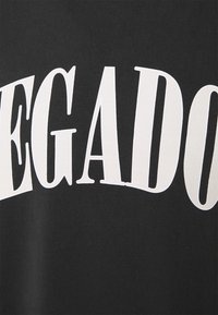 T-shirt nera con testo bold bianco che recita "LEGADO." Il tessuto ha una consistenza liscia e il design è centrato sul petto.