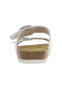 White sandal with a cork sole and two adjustable straps. Smooth finish with a flat heel and open back design. Silver hardware accents present.