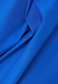 Tejido azul profundo con una textura mate y suave, que presenta suaves pliegues y arrugas, indicando flexibilidad y potencial de caídas.