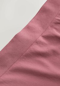 Pink stof med en struktureret, ribbet kant og glatte sektioner, der fremhæver en blød finish og en buet sømdetalje.