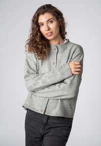 Light gray knitted sweater with a round neck, visible ribbed texture, and wooden button detail at the collar. Styled with black jeans.