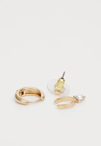 El conjunto de pendientes de tono dorado incluye un aro curvado, una pieza de perno con una base transparente y un diseño colgante con un acento de piedra en forma de lágrima.